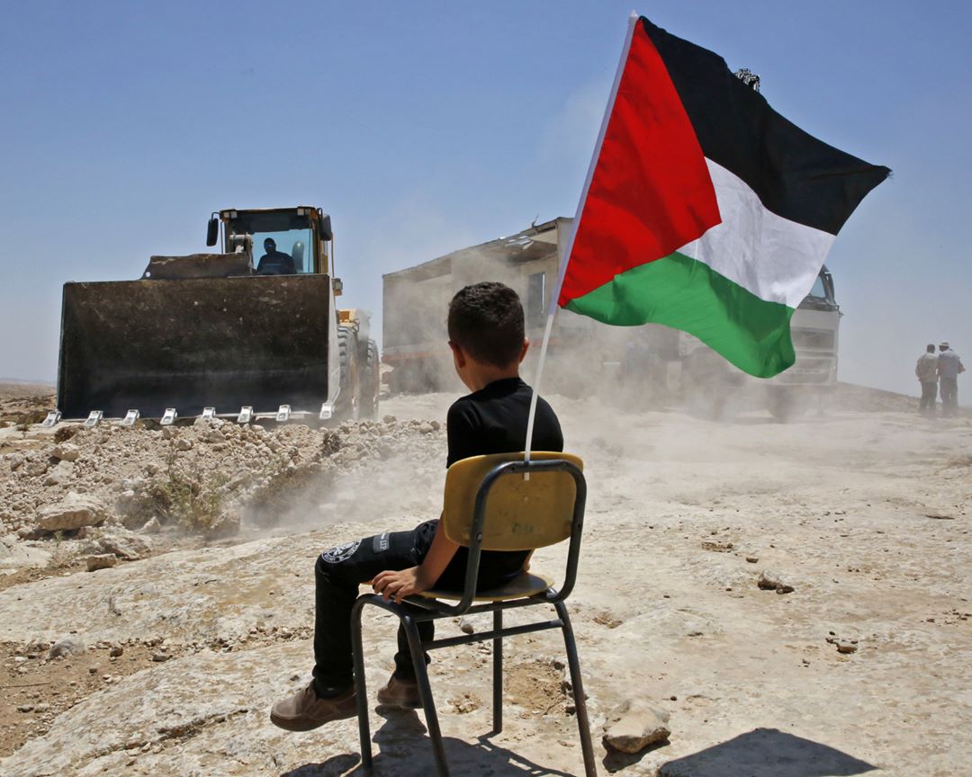 طفل فلسطيني قاعد على كرسي وشايل علم فلسطين